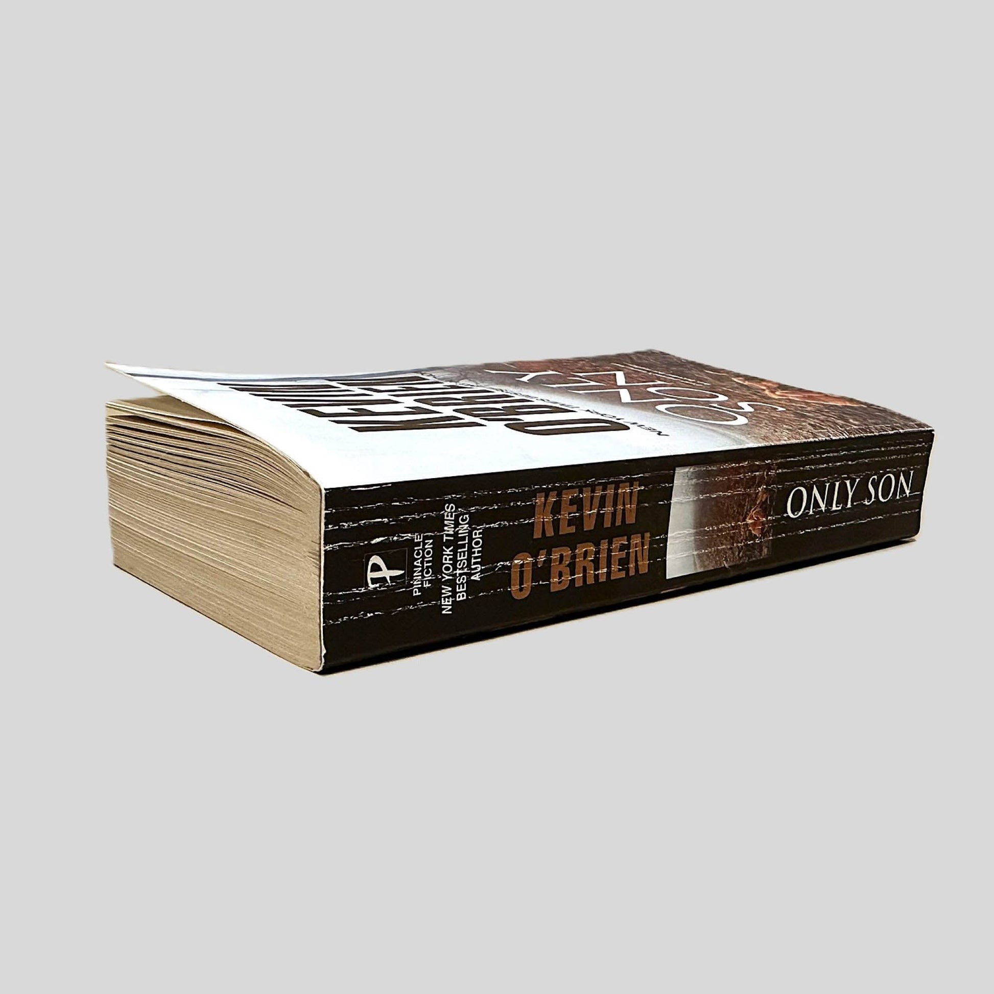 Close-up spine view of Only Son by Kevin O'Brien centered on a neutral light gray background. Spine shows creasing. Pages lay flat.