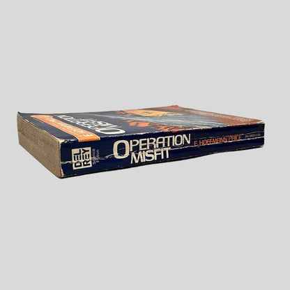 Close-up spine view of Operation Misfit by E. Hoffmann Price centered on a neutral light gray background. Spine is square; shows creasing and chipping at the corners. Pages lay flat.