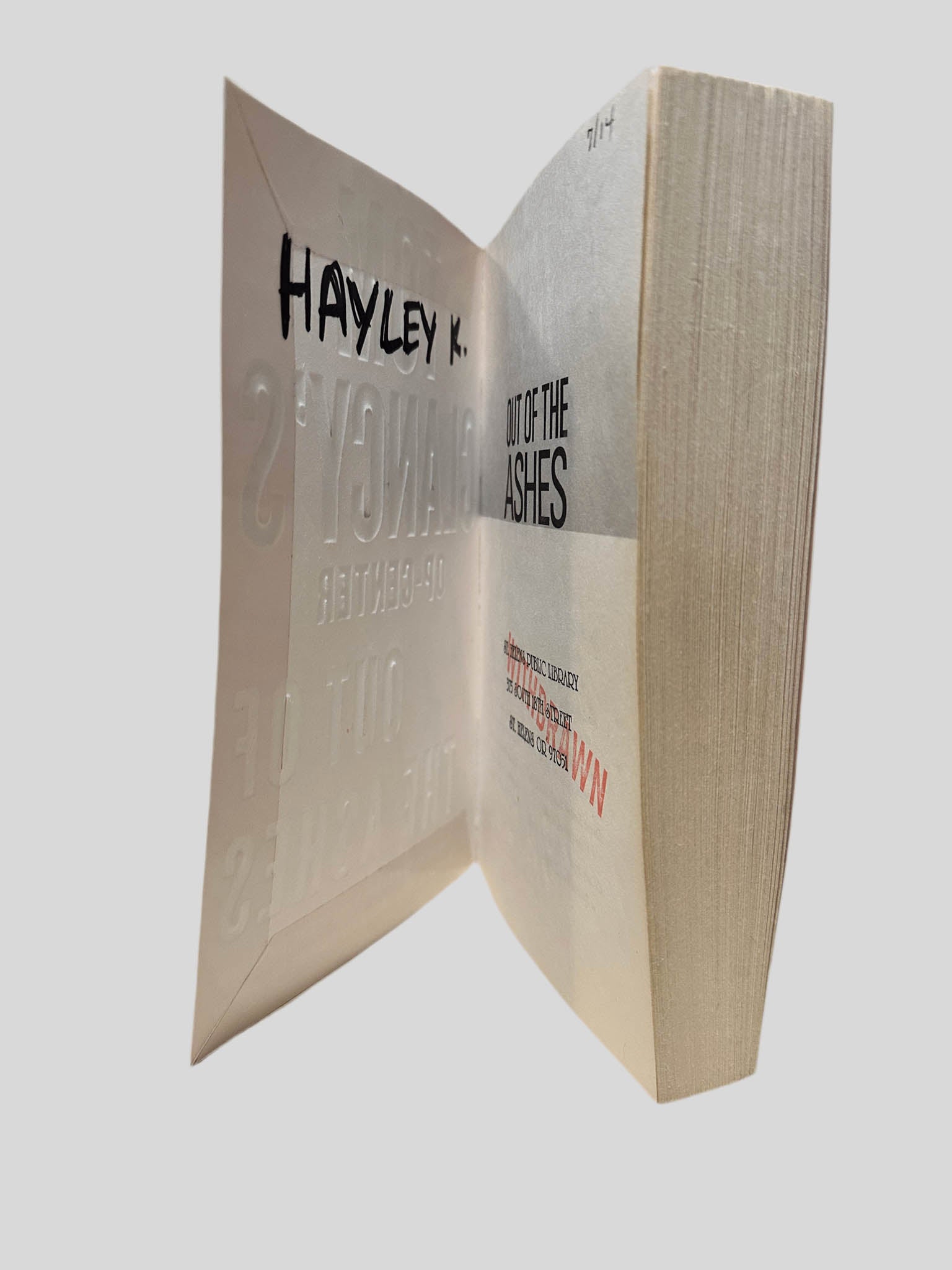 Inside front cover view of Out of the Ashes by Tom Clancy centered on a neutral light gray background. The name "HAYLEY K." is written on the inside front cover in black ink. "DISCARD" is stamped in red on the title page. Visible pages are straight and crisp.