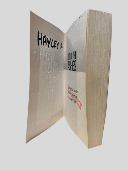 Inside front cover view of Out of the Ashes by Tom Clancy centered on a neutral light gray background. The name "HAYLEY K." is written on the inside front cover in black ink. "DISCARD" is stamped in red on the title page. Visible pages are straight and crisp.