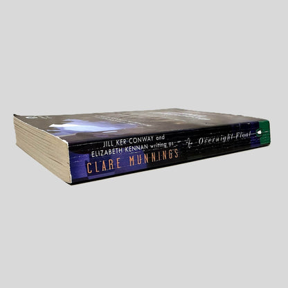 Close-up spine view of Overnight Float by Clare Munnings centered on a neutral light gray background. Spine shows creasing. Pages lay flat.