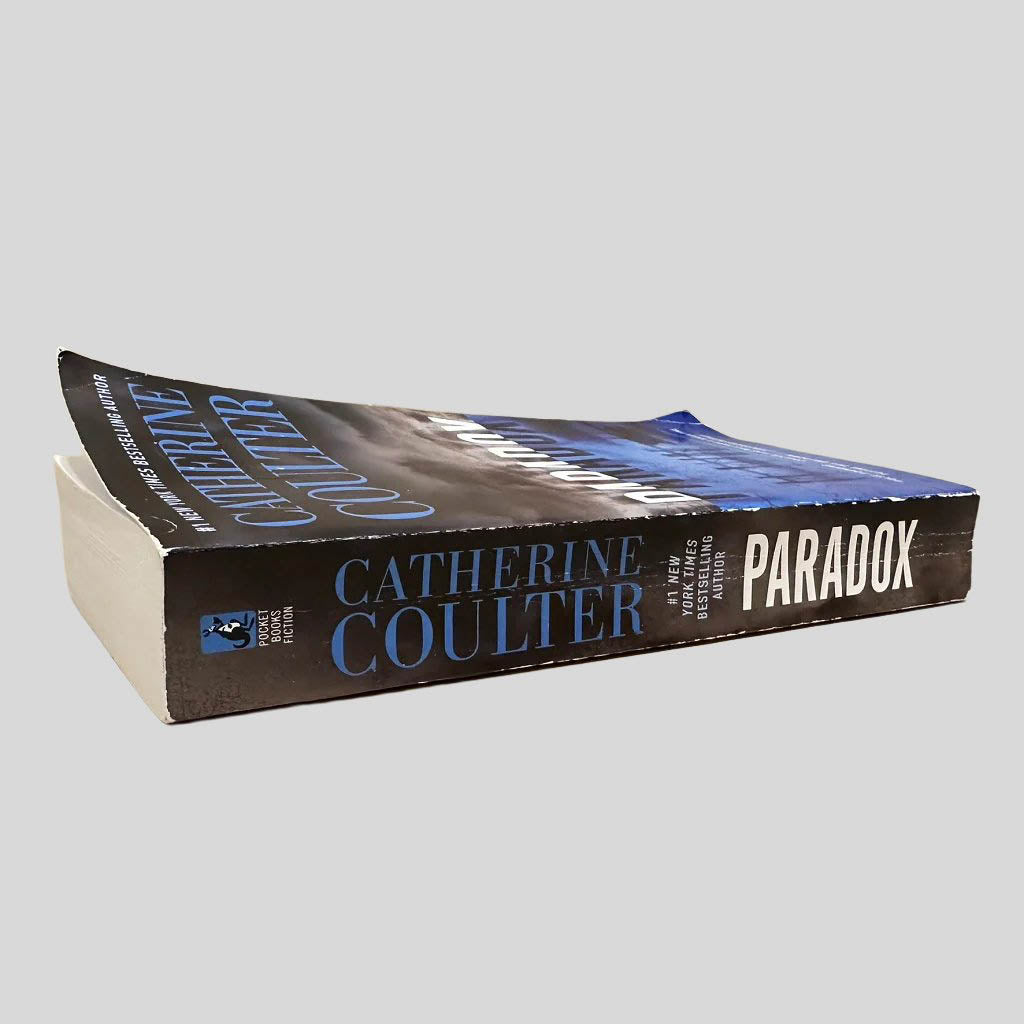 Close-up spine view of Paradox by Catherine Coulter centered on a neutral light gray background. Spine shows creasing.