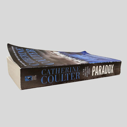 Close-up spine view of Paradox by Catherine Coulter centered on a neutral light gray background. Spine shows creasing.