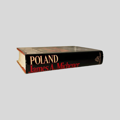 Close-up spine view of Poland A Novel by James A. Michener centered on a neutral light gray background. Dust jacket is present. Creasing on the top end of the jacket. Pages lay flat.