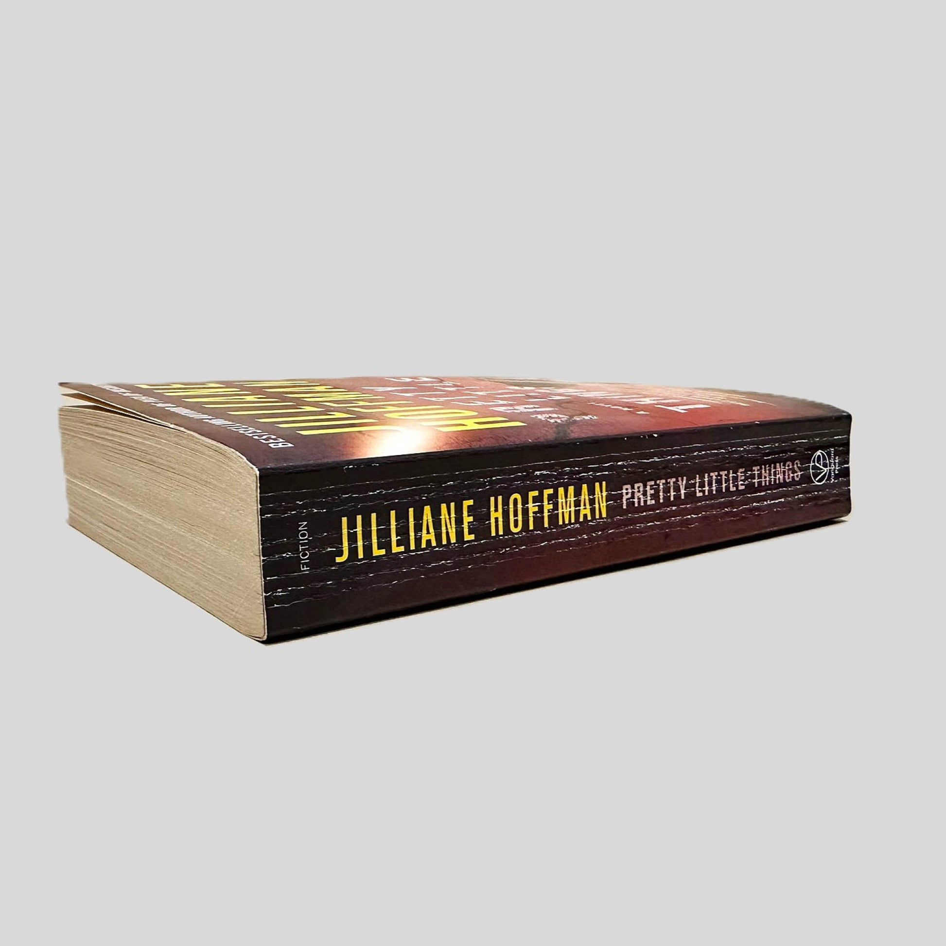 Close-up spine view of Pretty Little Things by Jilliane Hoffman centered on a neutral light gray background. Spine shows creasing.