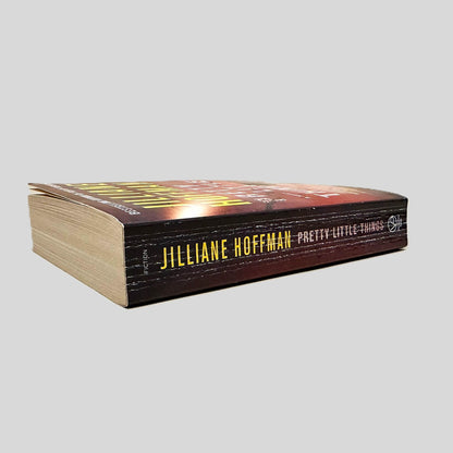 Close-up spine view of Pretty Little Things by Jilliane Hoffman centered on a neutral light gray background. Spine shows creasing.
