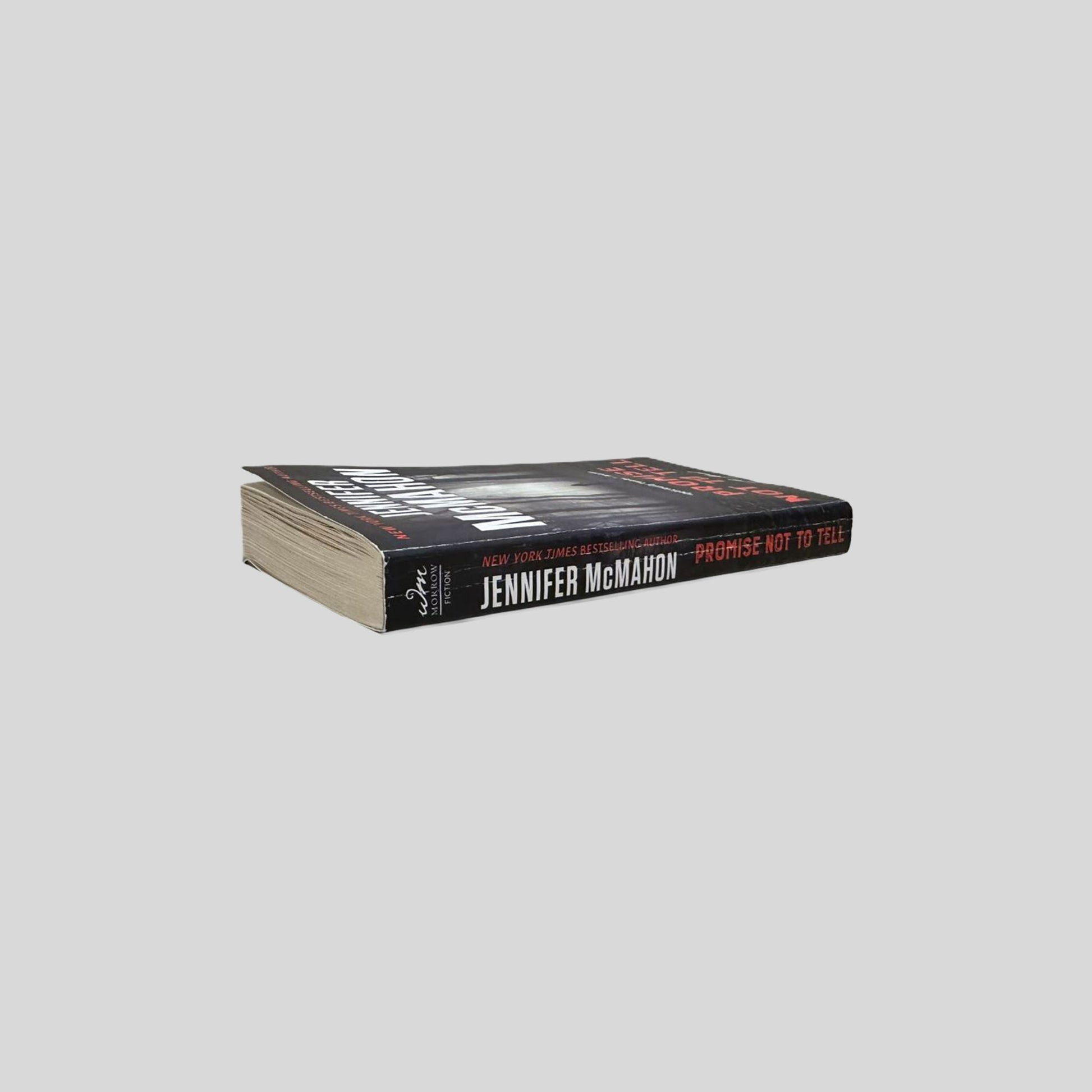 Close-up spine view of Promise Not To Tell by Jennifer McMahon centered on a neutral light gray background. 