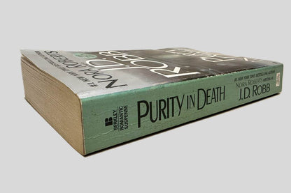 Close-up spine view of Purity in Death by J.D. Robb centered on a neutral light gray background. Spine shows minimal creasing. Pages lay flat.