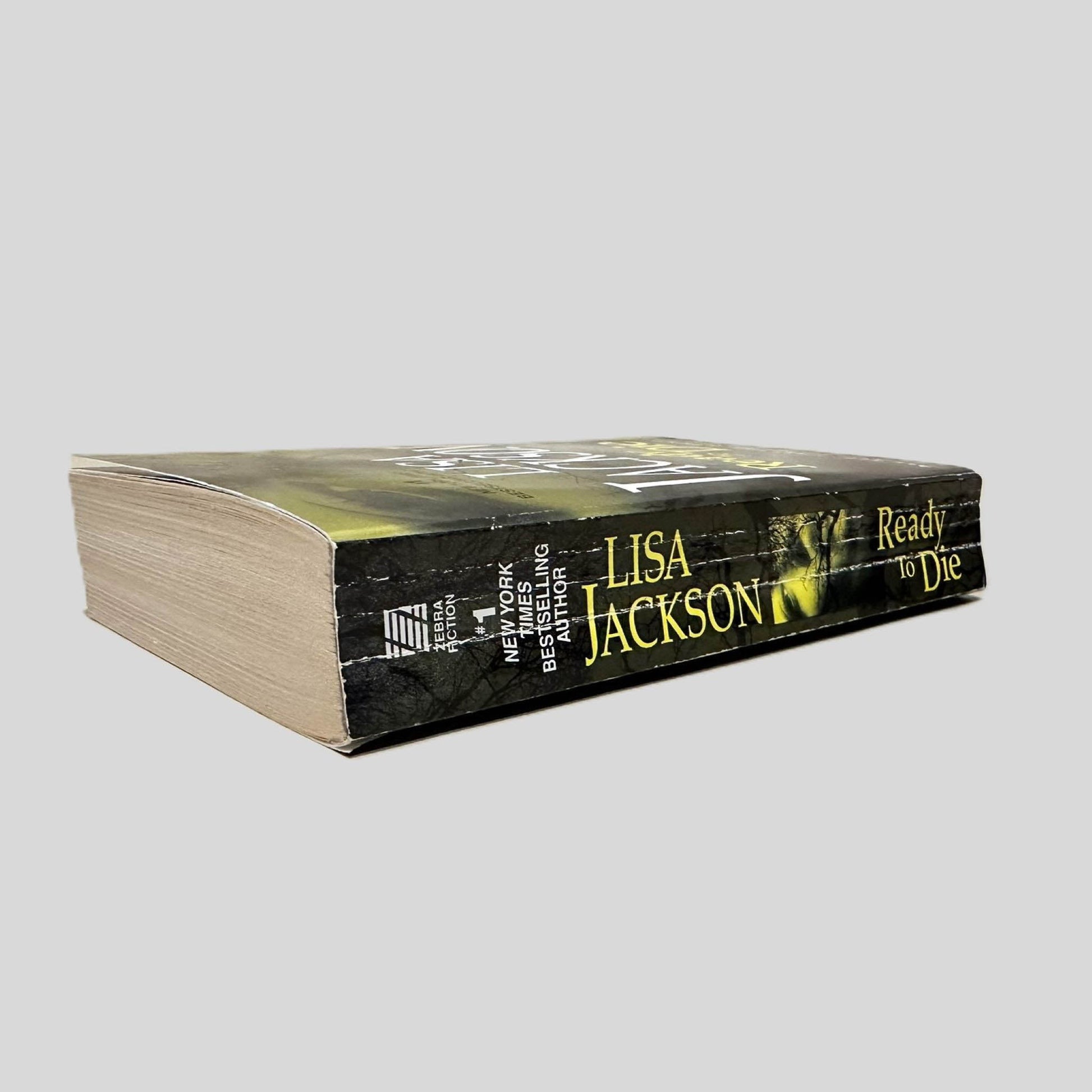 Close-up spine view of Ready to Die by Lisa Jackson centered on a neutral light gray background. Spine shows creasing. Pages lay flat.