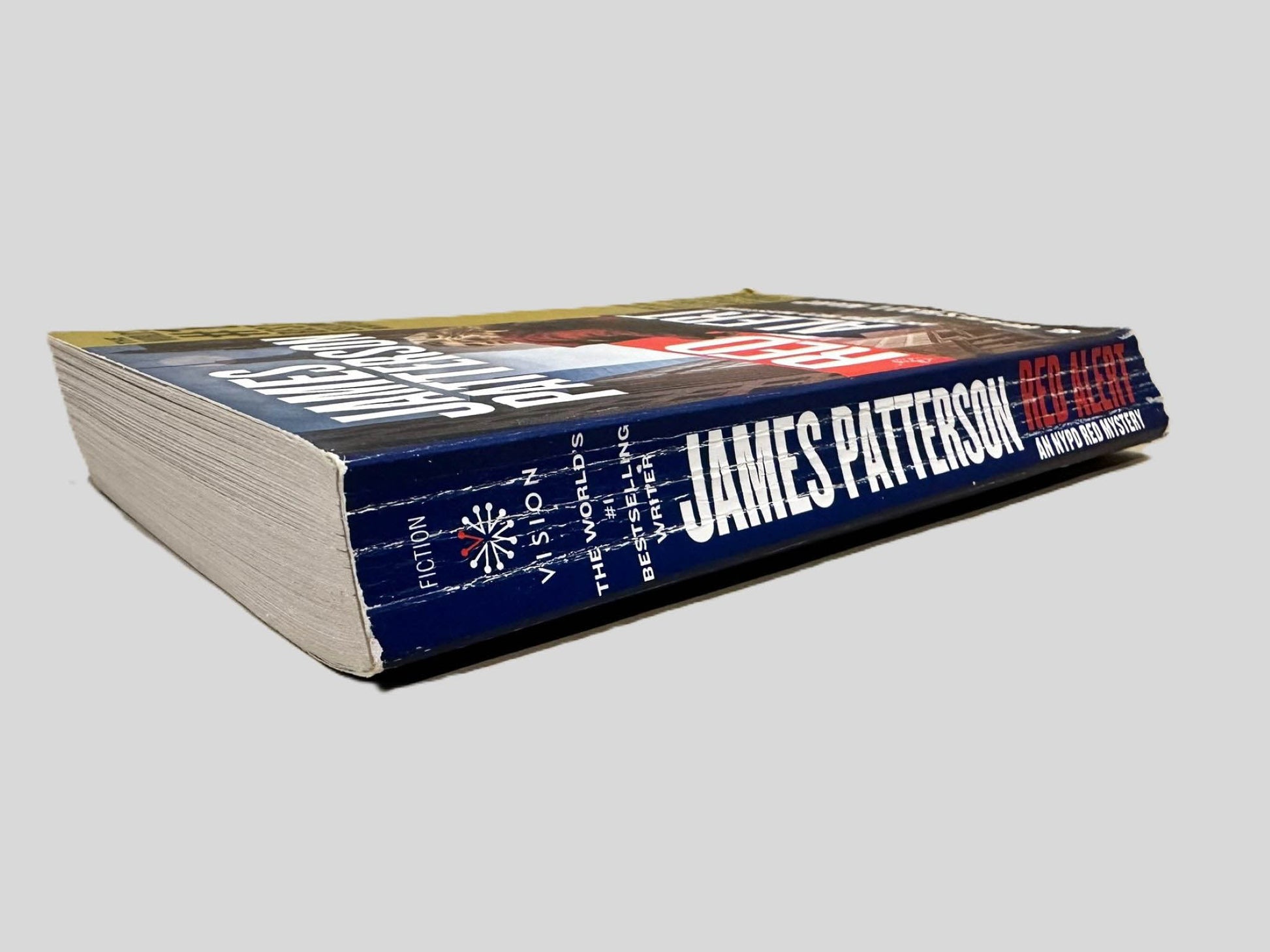 Close-up spine view of Red Alert by James Patterson centered on a neutral light gray background. Spine shows creasing, chipping and cocking.