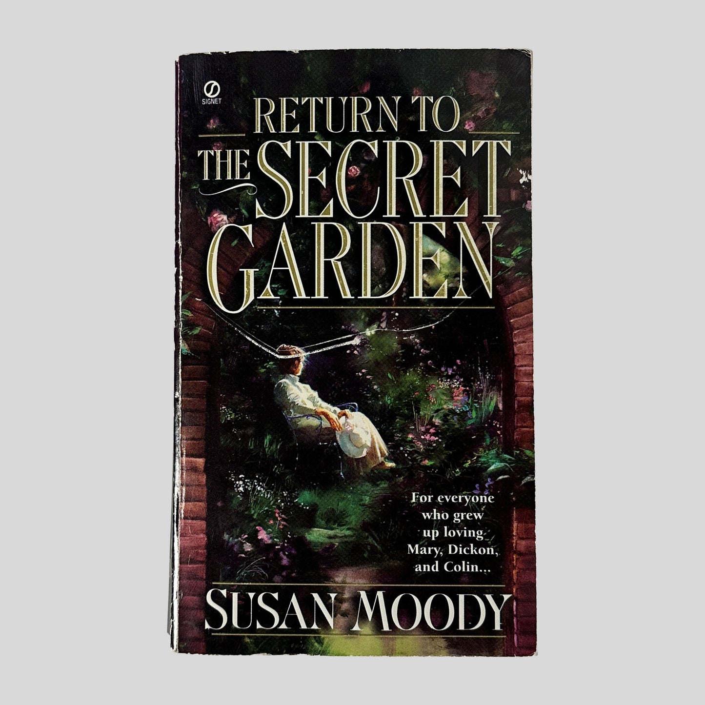 The front cover of the paperback Return to the Secret Garden by Susan Moody, featuring an illustration of a woman in white sitting in a sun-drenched, overgrown garden framed by a brick archway.