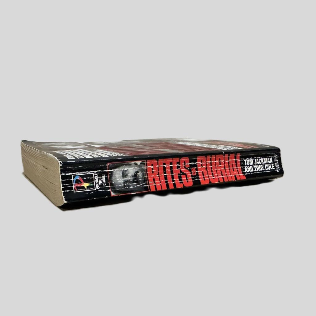 Close-up spine view of Rites of Burial by Tom Jackman & Troy Cole centered on a neutral light gray background. Spine shows creasing and slight cocking.