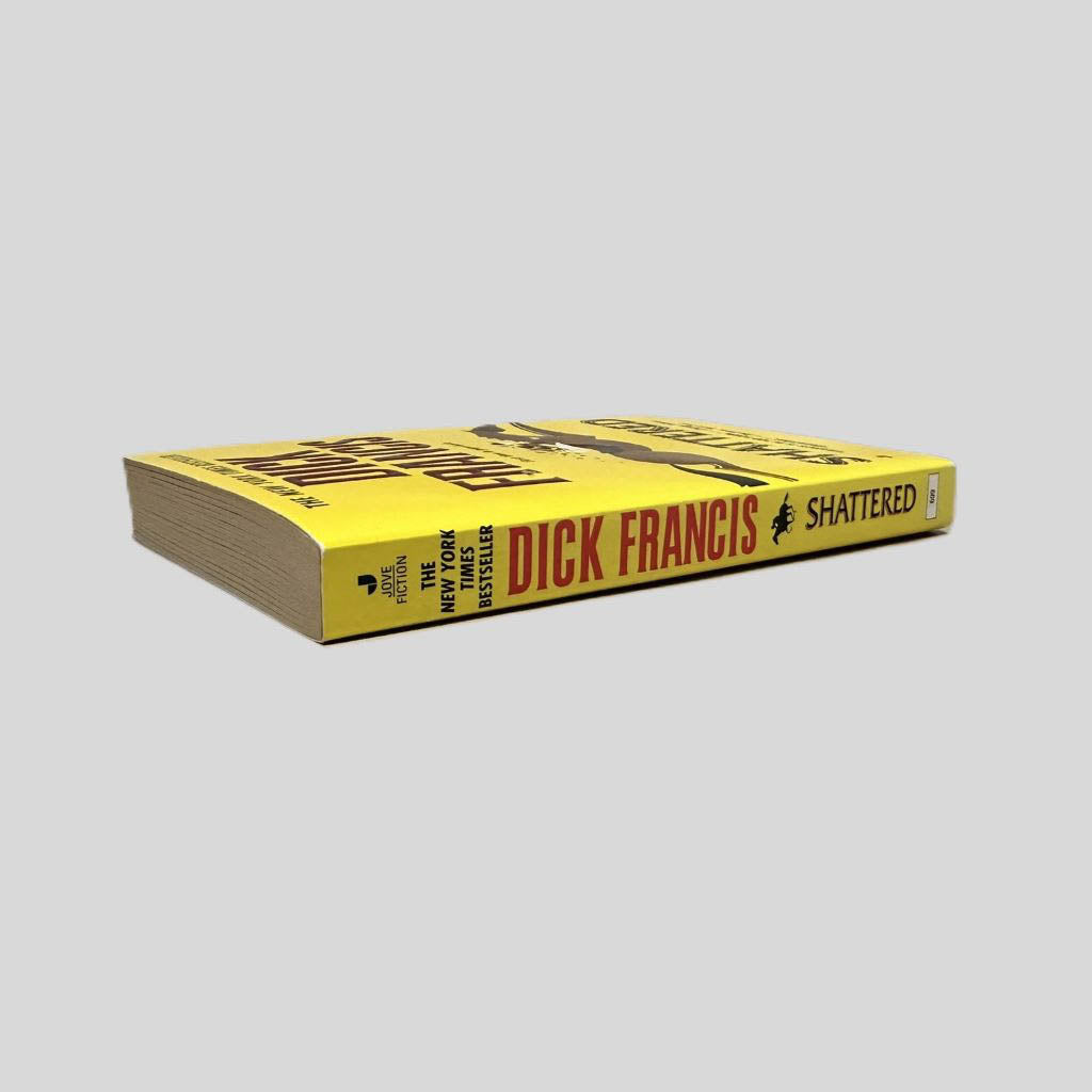 Close-up spine view of Shattered by Dick Francis centered on a neutral light gray background. Spine is square and shows minimal creasing.