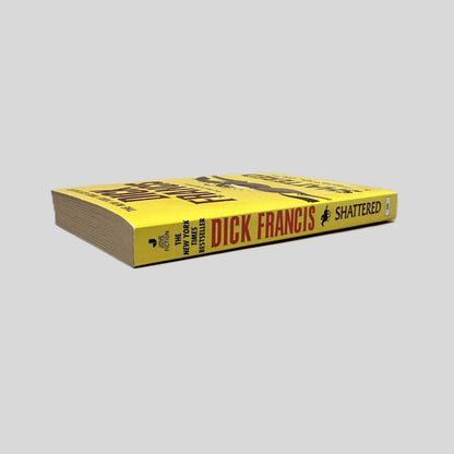 Close-up spine view of Shattered by Dick Francis centered on a neutral light gray background. Spine is square and shows minimal creasing.