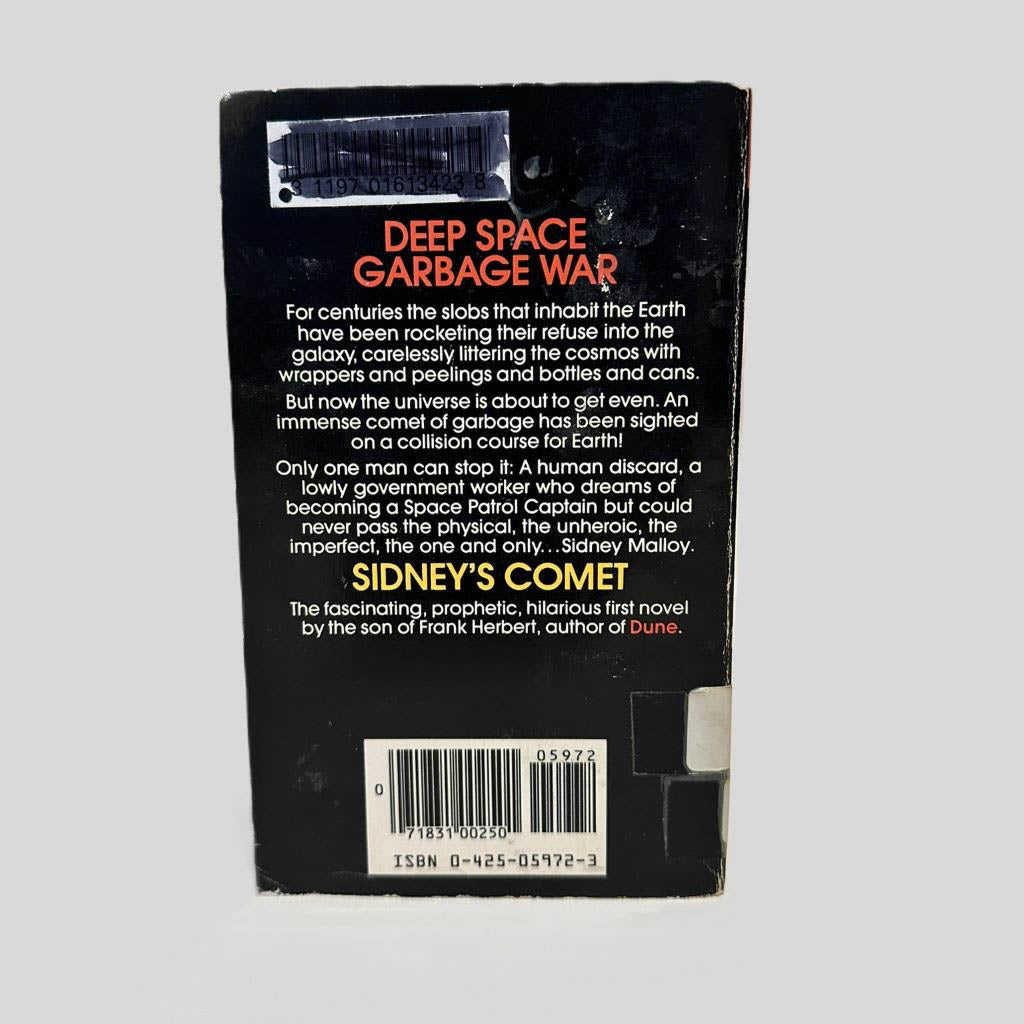 Back cover view of Sidney's Comet by Brian Herbert centered on a neutral light gray background. Chipping and creasing are present on the corners. Library barcode sticker in the top left corner, colored over with black ink. 