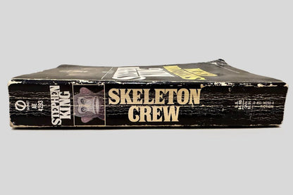 Close-up spine view of Skeleton Crew by Stephen King centered on a neutral light gray background. Creasing, chipping, rubbing present. Pages lay flat.