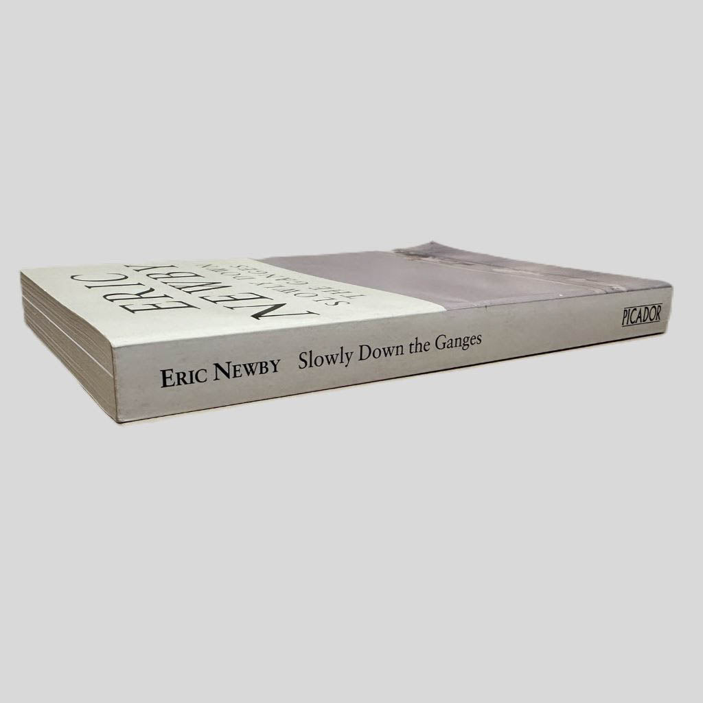 Close-up spine view of Slowly Down the Ganges by Eric Newby centered on a neutral light gray background. Spine is square and shows minimal creasing. Pages lay flat.