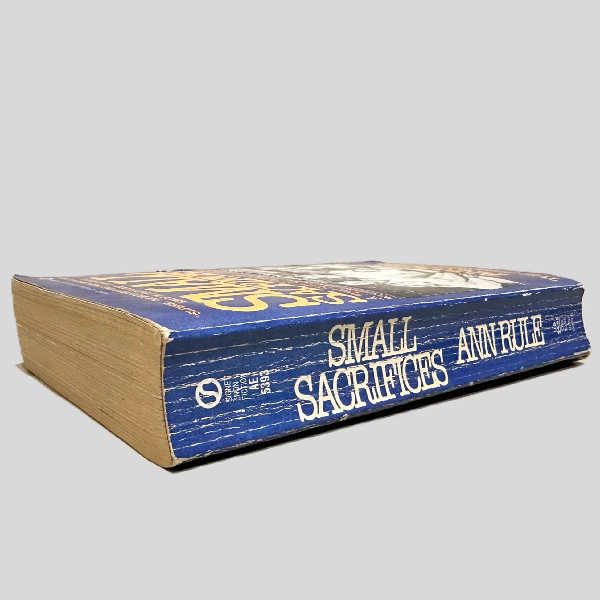 Close-up spine view of Small Sacrifices by Ann Rule centered on a neutral light gray background. Spine show creasing.