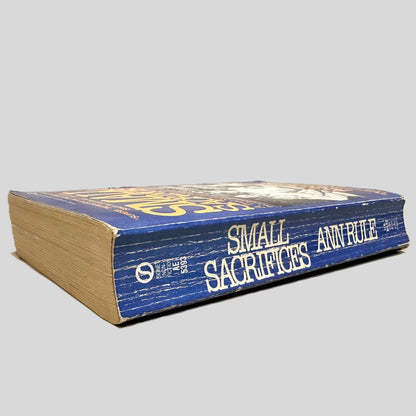 Close-up spine view of Small Sacrifices by Ann Rule centered on a neutral light gray background. Spine show creasing.