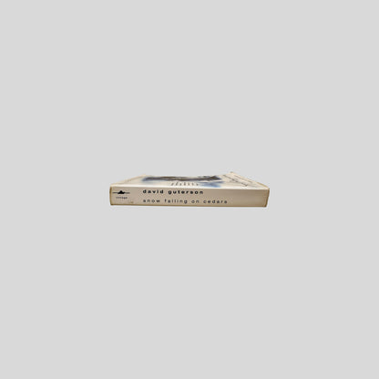 Close-up spine view of Snow Falling On Cedars by David Guterson centered on a neutral light gray background. 