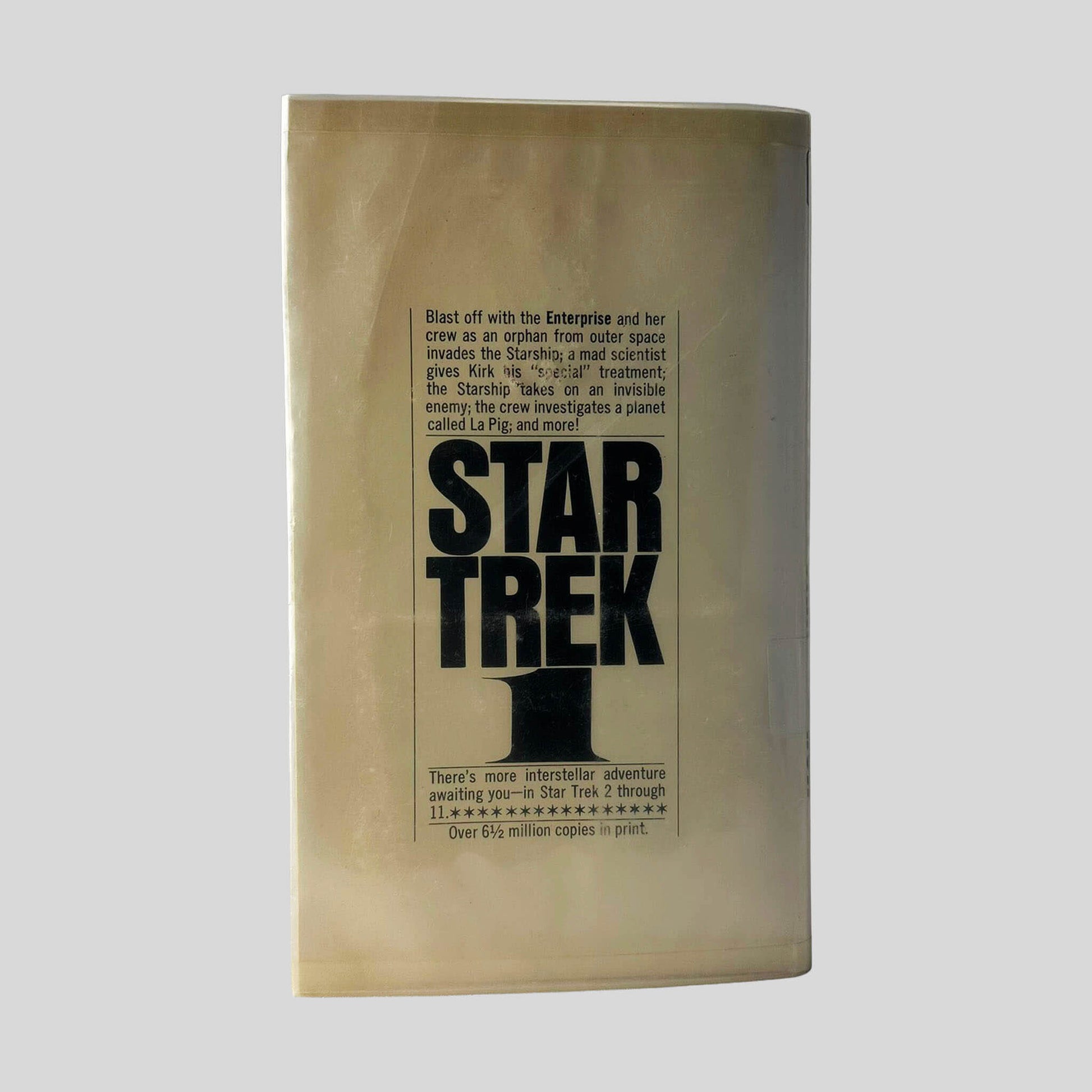 Back cover view of Star Trek 1 adapted by James Blish centered on a neutral light gray background. Library mylar cover is present to protect the book. No noteable damage.
