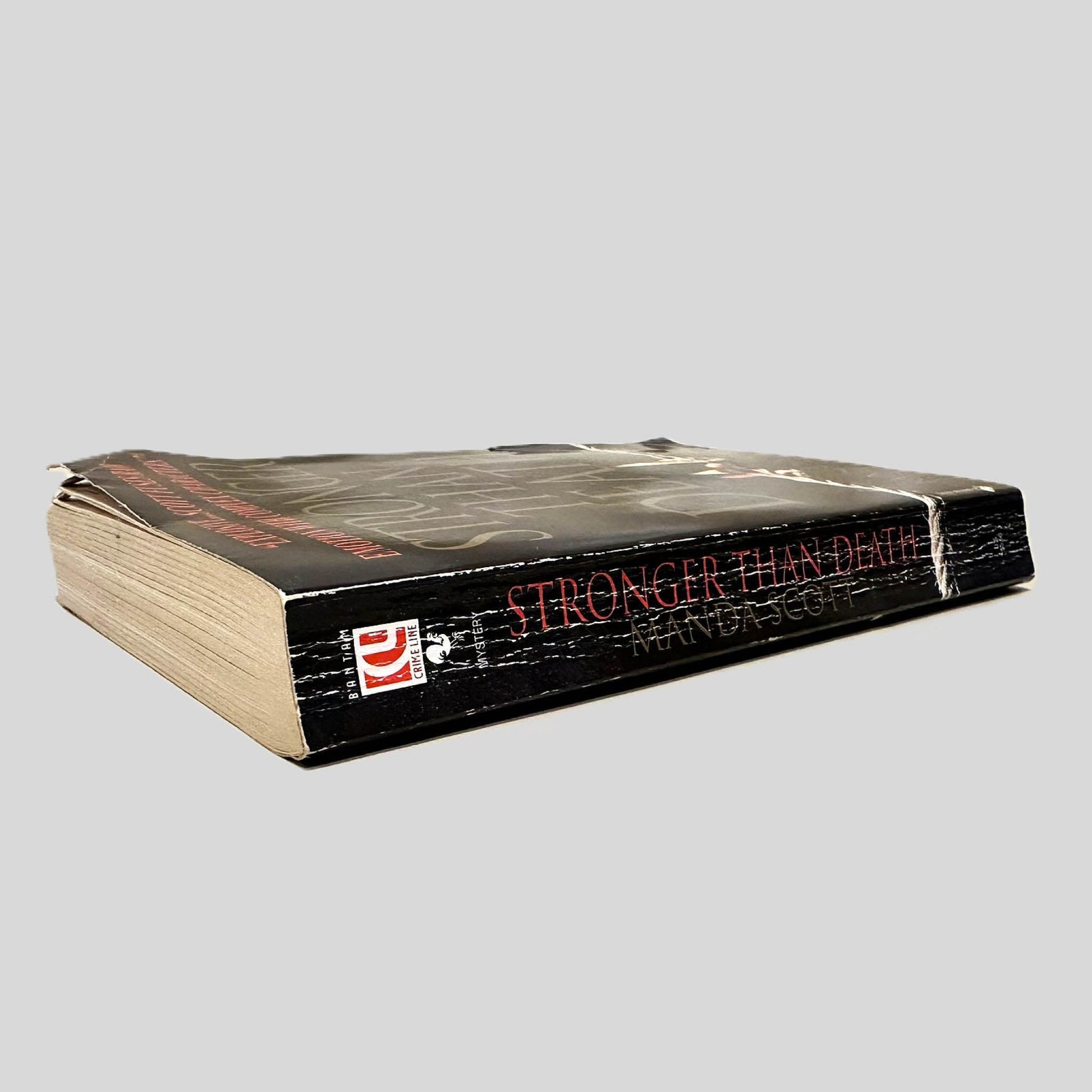 Close-up spine view of Stronger Than Death by Manda Scott centered on a neutral light gray background. Spine shows creasing and bumping to the outer page corner. Pages all otherwise lay flat.