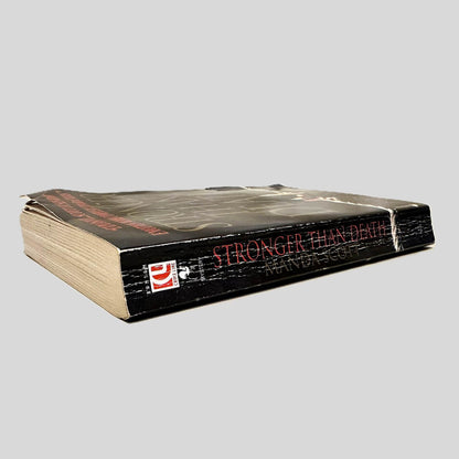 Close-up spine view of Stronger Than Death by Manda Scott centered on a neutral light gray background. Spine shows creasing and bumping to the outer page corner. Pages all otherwise lay flat.