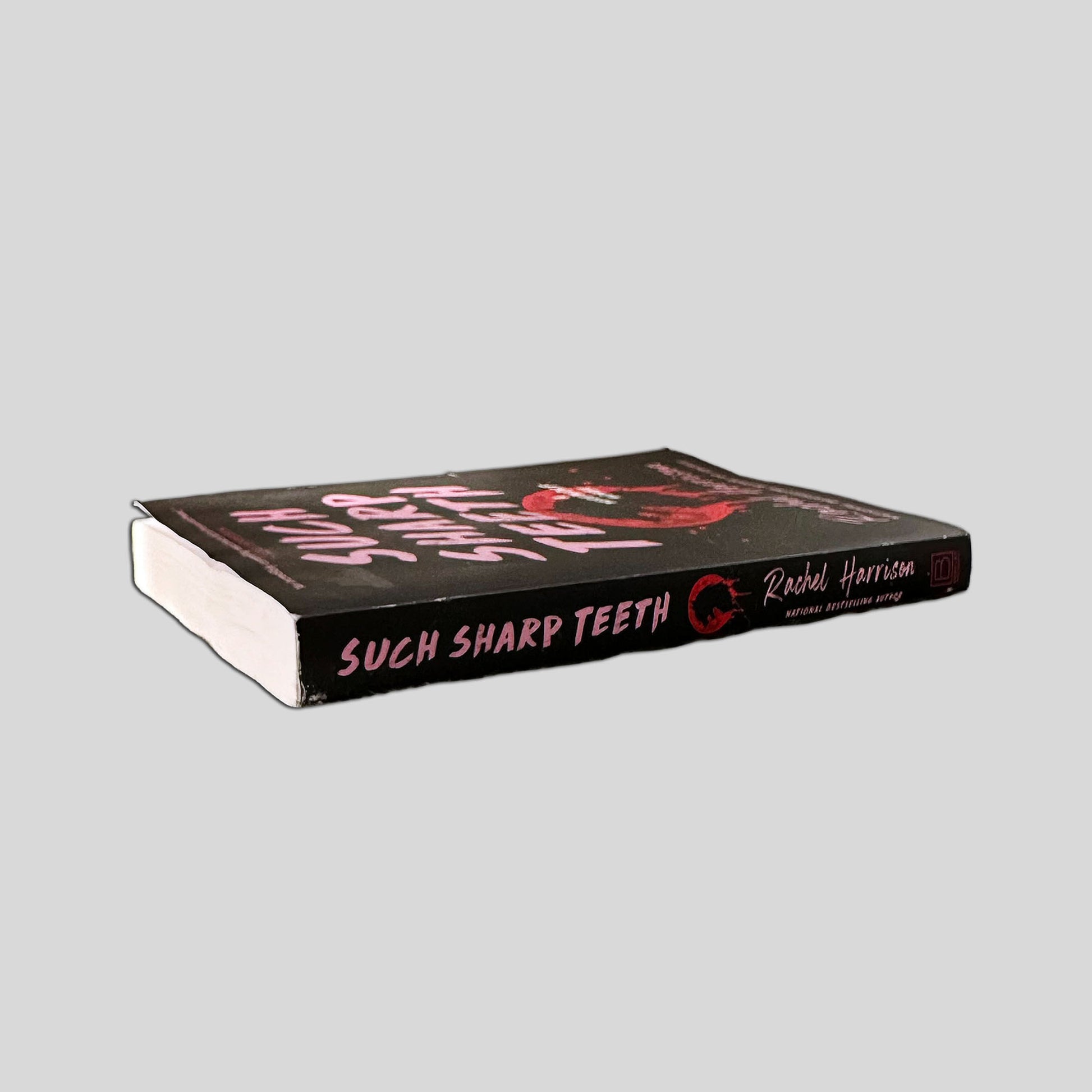 Close-up spine view of Such Sharp Teeth by Rachel Harrison centered on a neutral light gray background. 