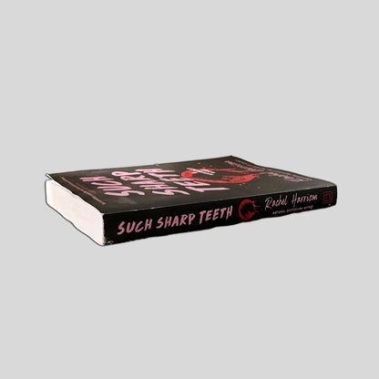 Close-up spine view of Such Sharp Teeth by Rachel Harrison centered on a neutral light gray background. 