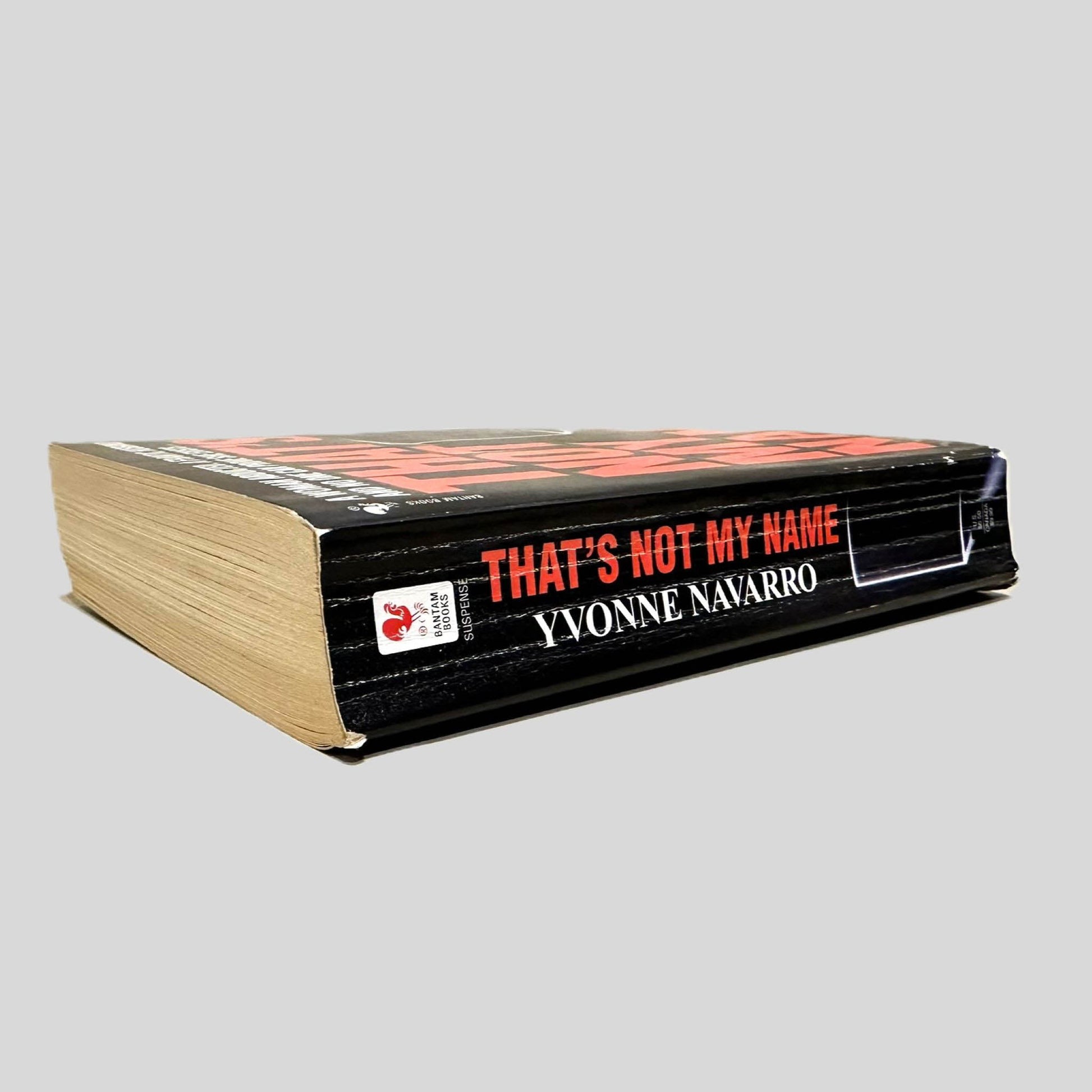 Close-up spine view of That's Not My Name by Yvonne Navarro centered on a neutral light gray background. Spine shows creasing.