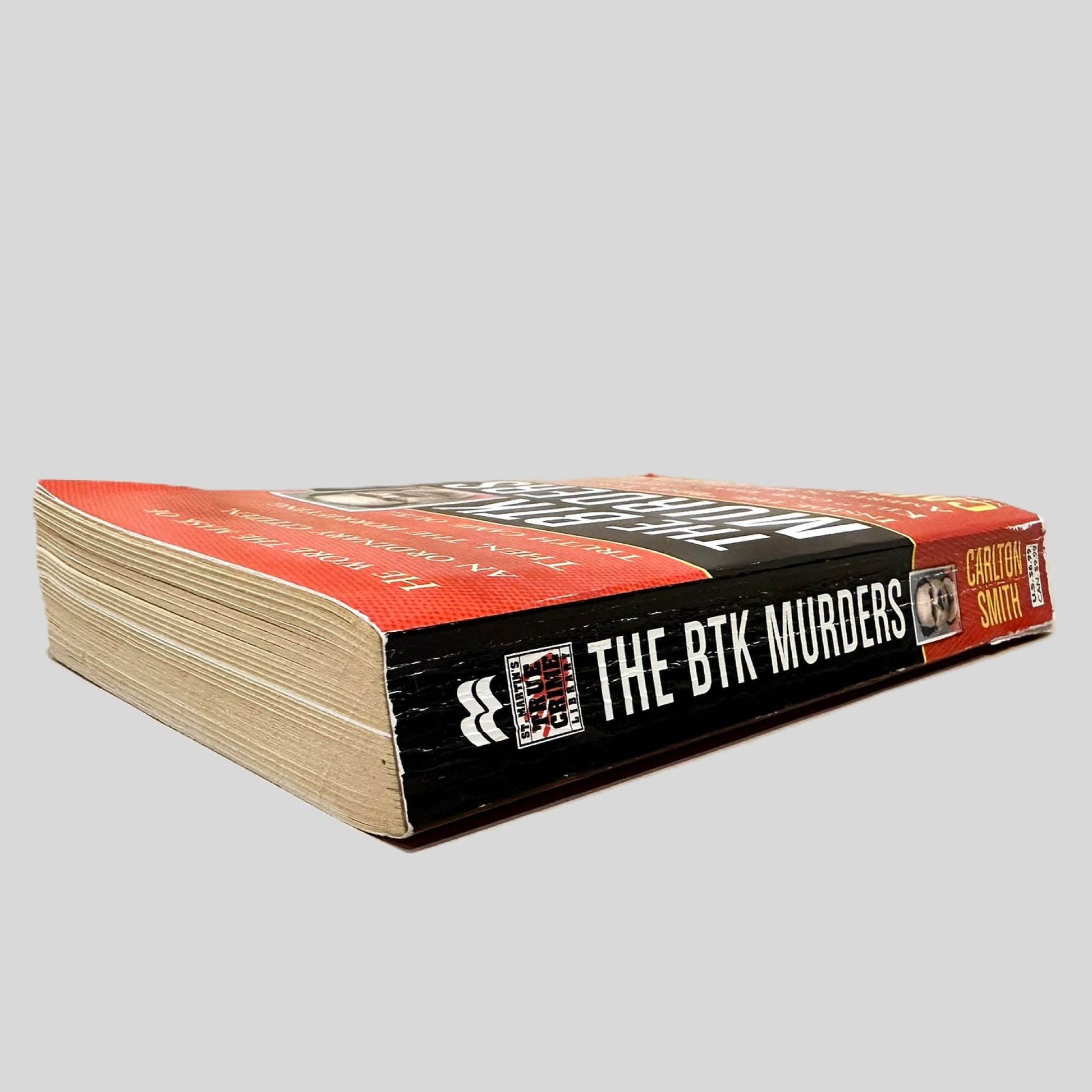 Close-up spine view of The BTK Murders by Carlton Smith centered on a neutral light gray background. Spine shows creasing and chipping.