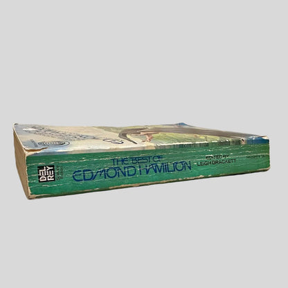 Close-up spine view of The Best of Edmond Hamilton edited by Leigh Brackett centered on a neutral light gray background. Spine is square; shows creasing and chipping to the top and lower end of the spine. Pages lay flat.
