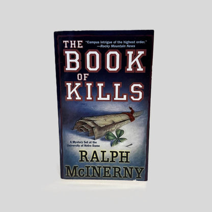 Front cover view of The Book of Kills by Ralph McInerny centered on a neutral light gray background. Minor chip on the bottom right of the front cover.