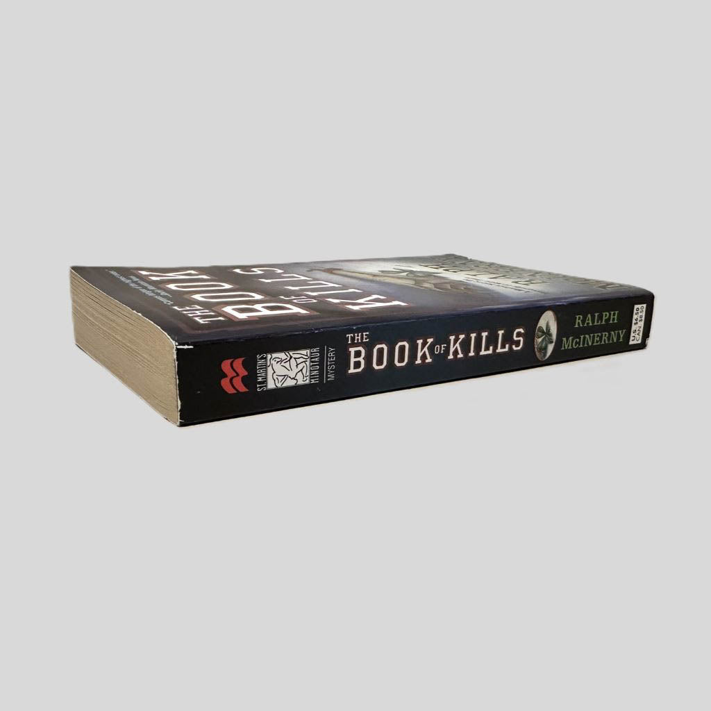 Close-up spine view of The Book of Kills by Ralph McInerny centered on a neutral light gray background. Spine is square and shows no creasing. Pages lay flat.