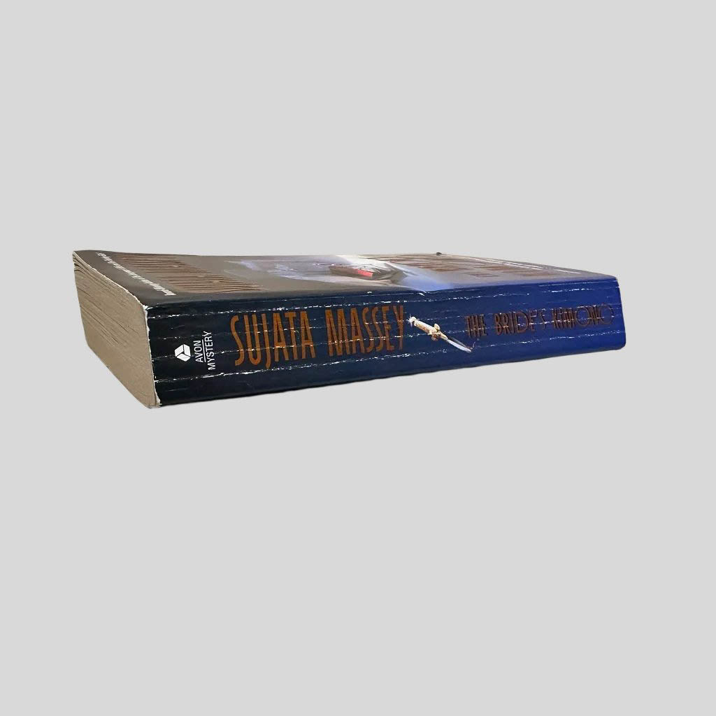 Close-up spine view of The Bride's Kimono by Sujata Massey centered on a neutral light gray background. Spine shows creasing. Pages lay flat.