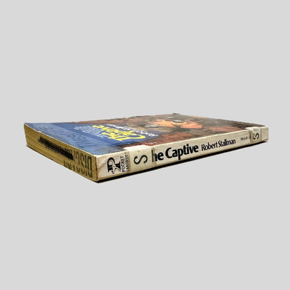 Close-up spine view of The Captive by Robert Stallman centered on a neutral light gray background. Spine shows creasing and bumping. Discard is stamped across the top page edge. The letter "S" is taped once to the top of the spine and again at the bottom for library cataloging. Pages lay flat.