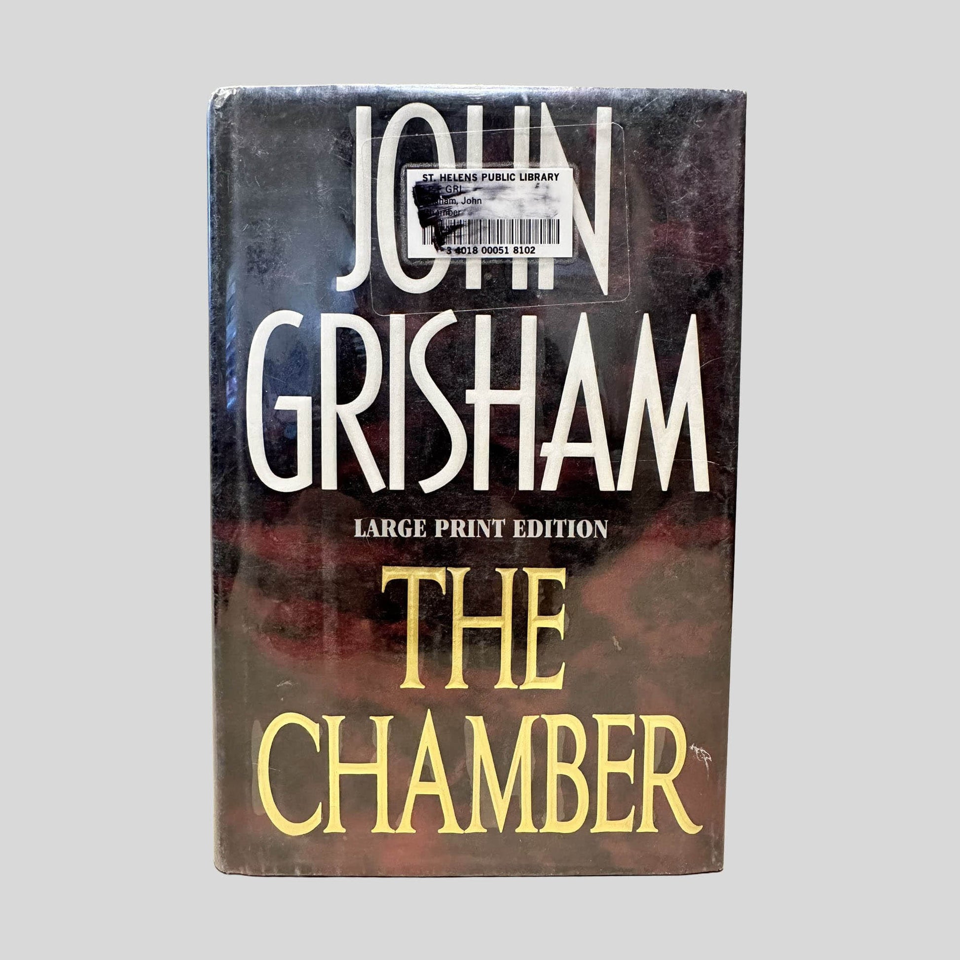 Front cover view of The Chamber by John Grisham (Large Print Edition) centered on a neutral light gray background. Mylar covered dust jacket is present. St. Helens Public Library barcode sticker with black ink over it is attached to the top center, covering part of the author's name.