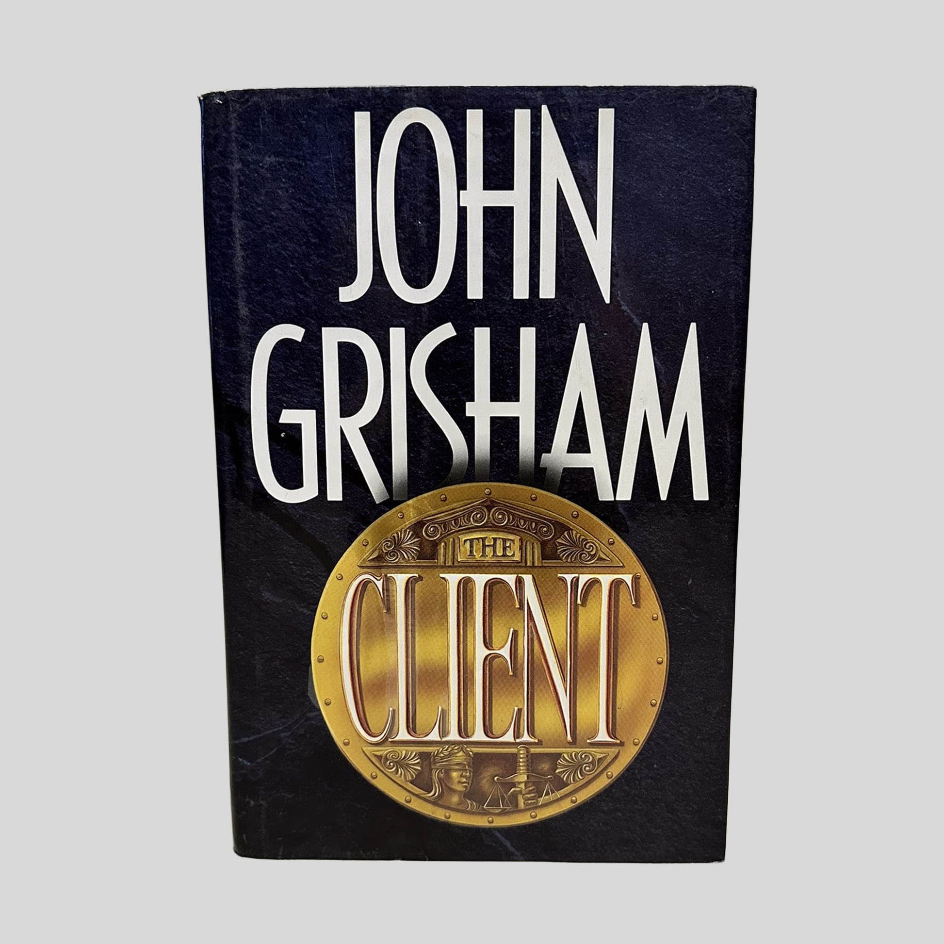 Front cover view of The Client by John Grisham centered on a neutral light gray background. Dust jacket is present and shows normal wear.