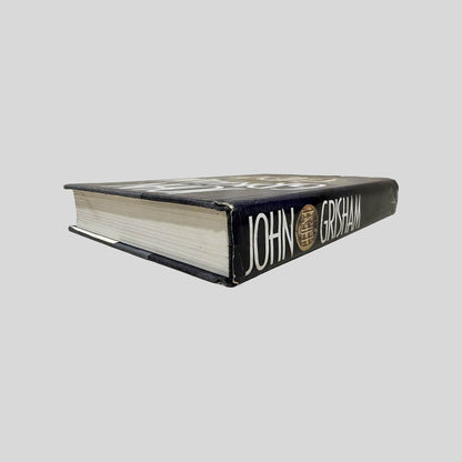 Close-up spine view of The Client by John Grisham centered on a neutral light gray background. Dust jacket is present and shows normal wear. Pages lay flat.
