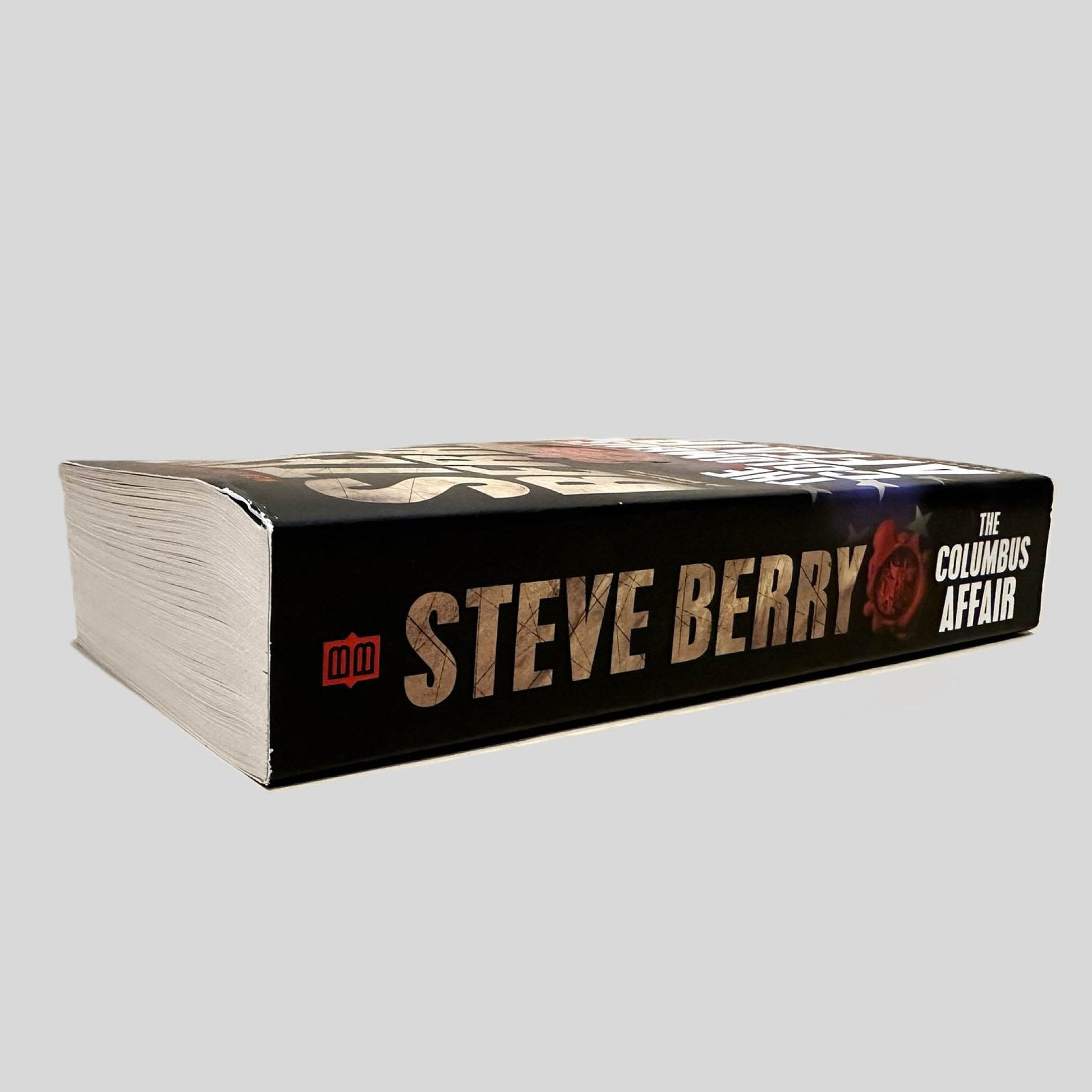 Close-up spine view of The Columbus Affair by Steve Berry centered on a neutral light gray background. Spine is square and shows no visible creasing. Pages lay flat.