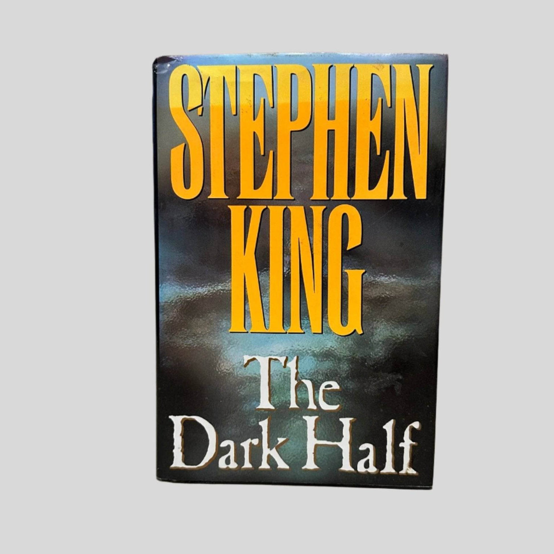 Front cover view of The Dark Half by Stephen King centered on a neutral light gray background. Dust jacket is present. Small tear in the top left corner.