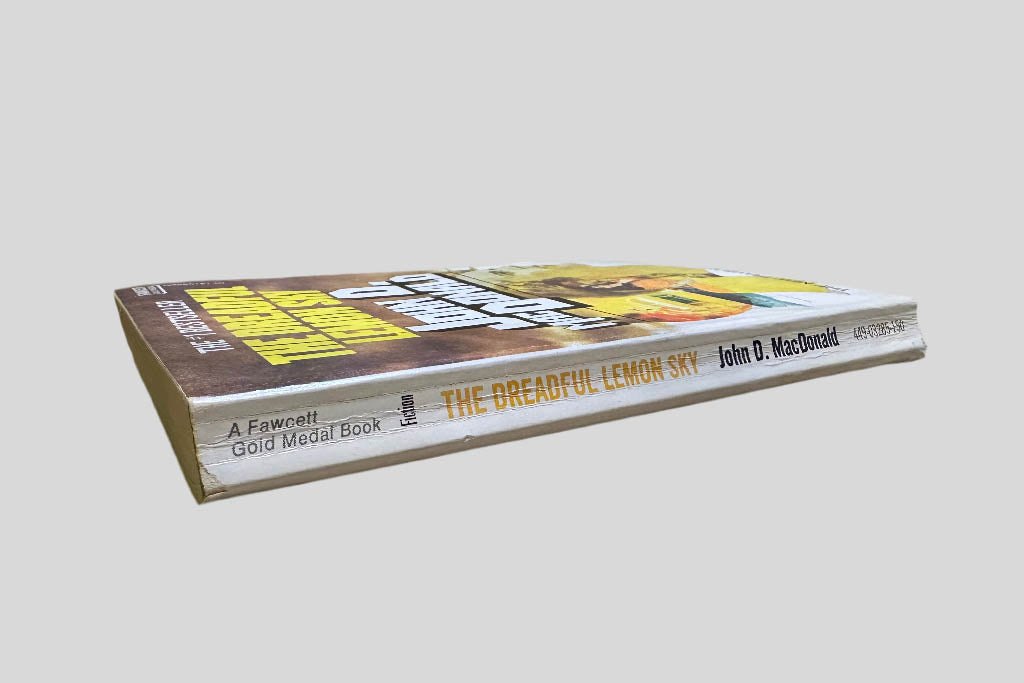 Close-up spine view of The Dreadful Lemon Sky by John D. MacDonald centered on a neutral light gray background. Spine shows creasing.