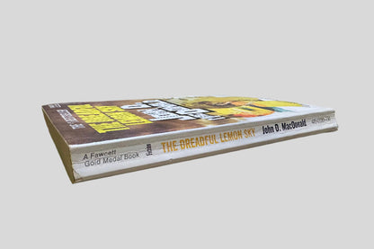 Close-up spine view of The Dreadful Lemon Sky by John D. MacDonald centered on a neutral light gray background. Spine shows creasing.