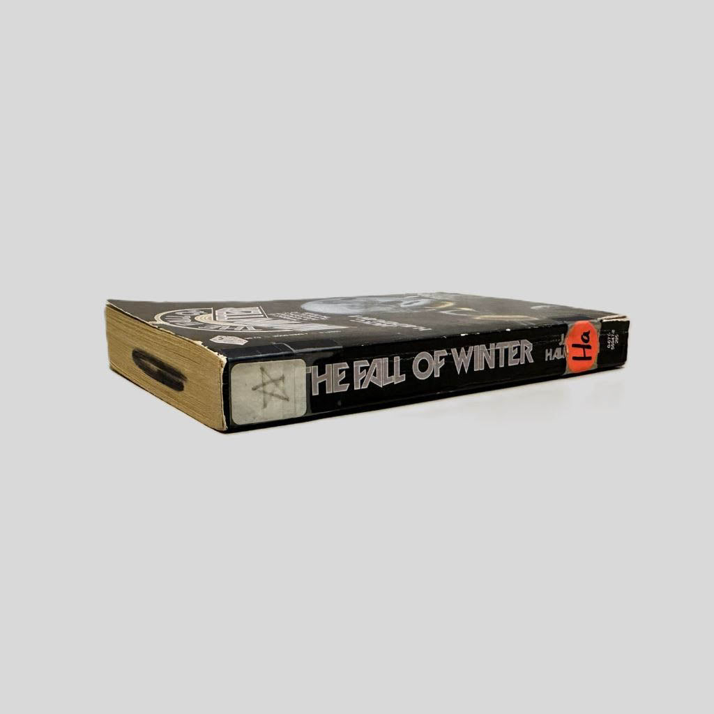 Close-up spine view of The Fall of Winter by Jack C. Haldeman II centered on a neutral light gray background. Spine is square and  shows minimal creasing. Library shelving stickers are present at the top and lower end of the spine. Pages lay flat.