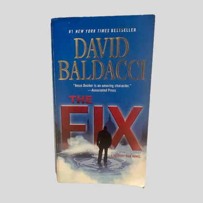 Front cover view of The Fix by David Baldacci centered on a neutral light gray background. Bottom right corner shows chipping.