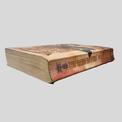 Close-up spine view of The Game Beyond by Melissa Scott centered on a neutral light gray background. Spine shows creasing. Pages lay flat.
