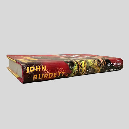 Close-up spine view of The Godfather of Kathmandu by John Burdett centered on a neutral light gray background.  Dust jacket present and undamaged.