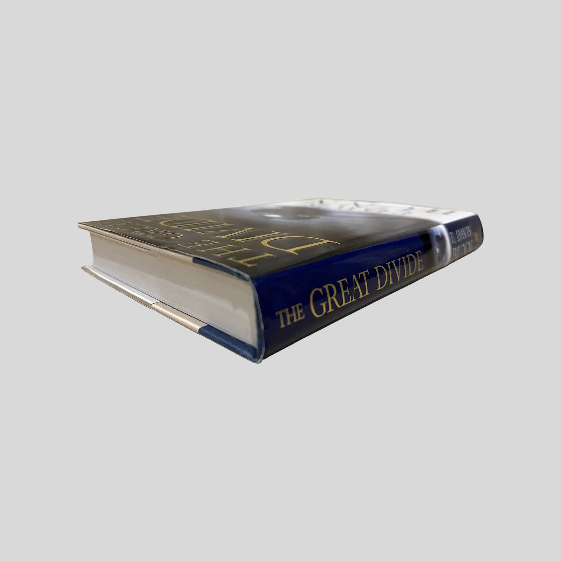 Close-up spine view of The Great Divide by T. Davis Bunn centered on a neutral light gray background. Dust jacket is present and no damage present. Spine shows no creasing. Pages lay flat.