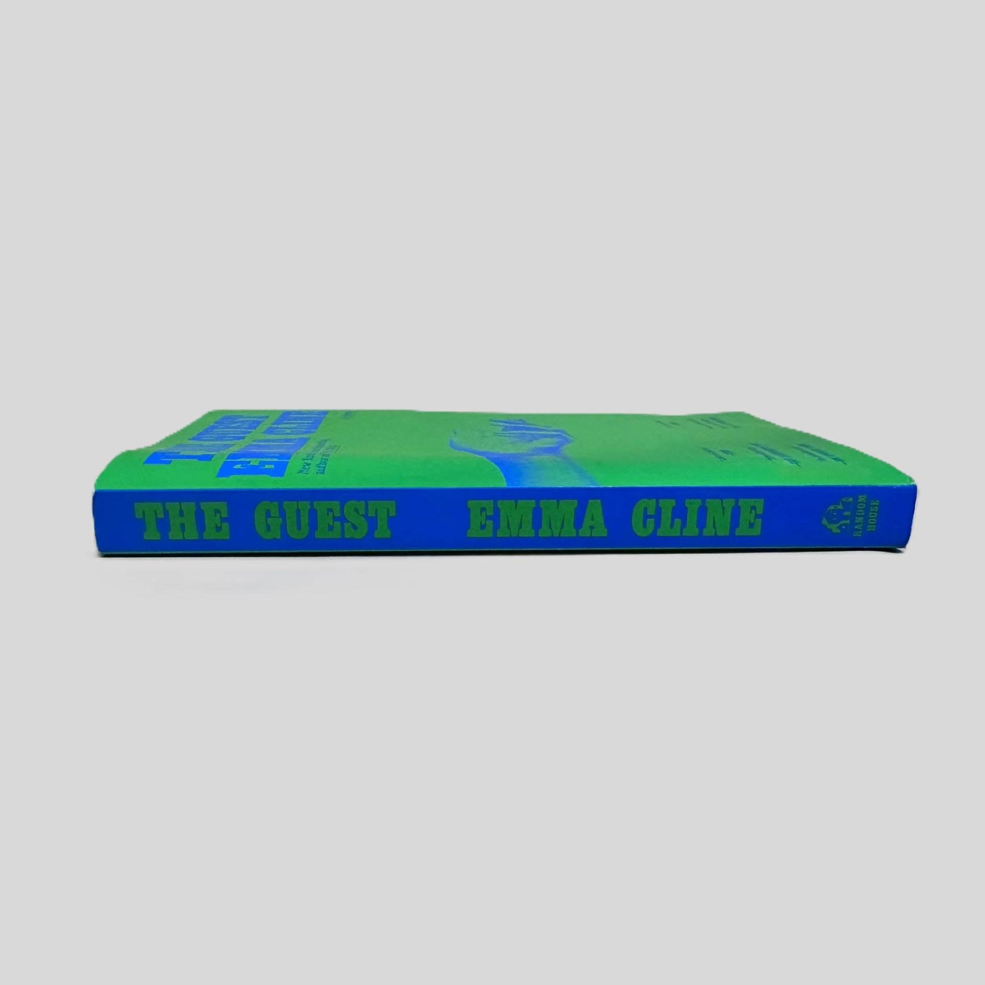 Close-up spine view of The Guest by Emma Cline centered on a neutral light gray background. Spine is square and shows no creasing. Pages lay flat.