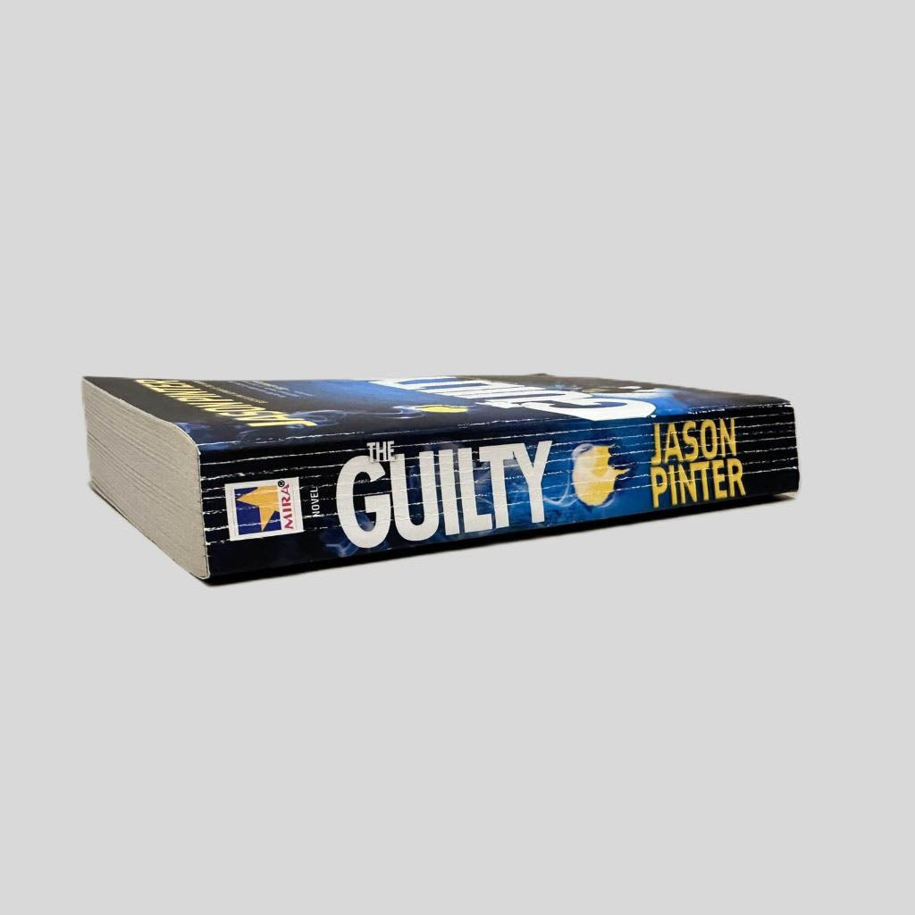 Close-up spine view of The Guilty by Jason Pinter centered on a neutral light gray background. Spine shows creasing. Pages lay flat.
